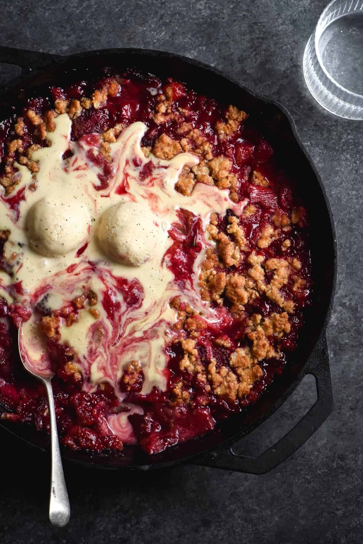 An overhead shot of a gluten free rhubarb and strawberry crumble topped with melting homemade vanilla ice cream.