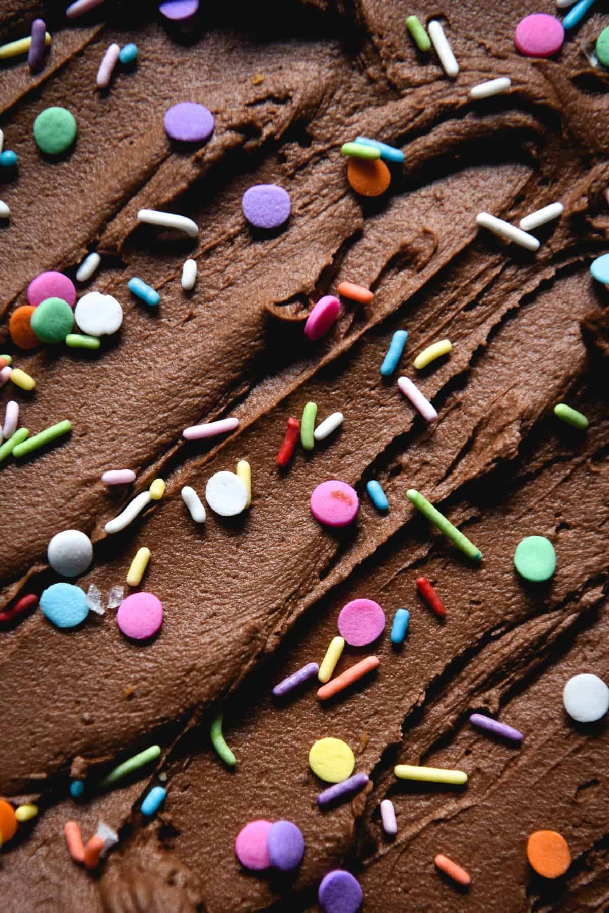 A close up of chocolate buttercream swirls topped with rainbow jimmies and round sprinkles