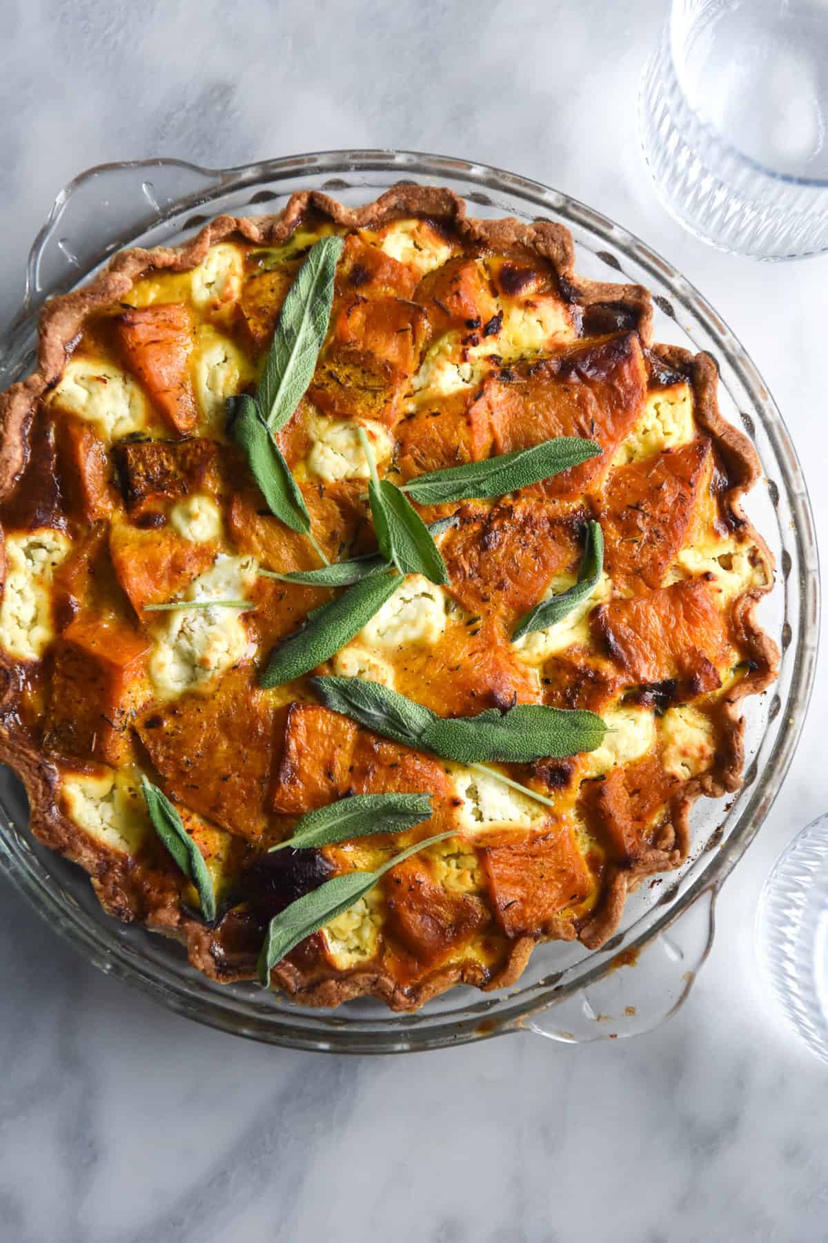 An aerial image of a pumpkin, sage and goat's cheese tart on a white marble table.