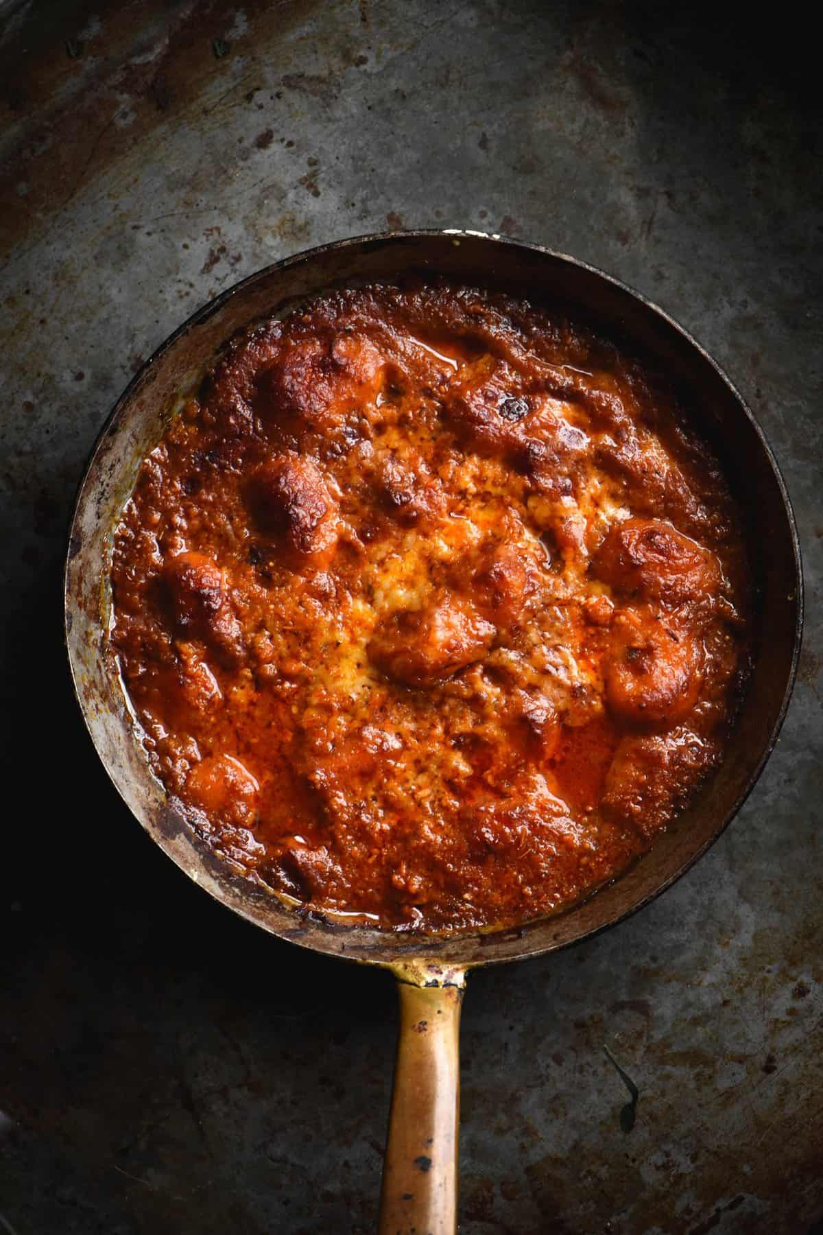 A small skillet of gluten free potato gnocchi baked in a rich FODMAP friendly pasta sauce and topped with melted cheese. The skillet sits against a dark grey metal backdrop.