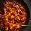 A close up of a small skillet of FODMAP friendly pasta sauce baked with gluten free potato gnocchi. A fork dips into the gnocchi in the bottom right hand side of the image.
