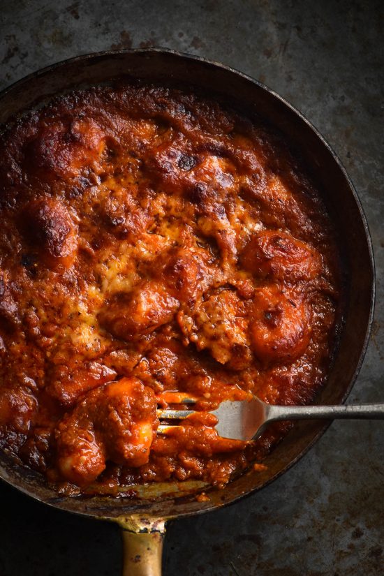 A close up of a small skillet of FODMAP friendly pasta sauce baked with gluten free potato gnocchi. A fork dips into the gnocchi in the bottom right hand side of the image.