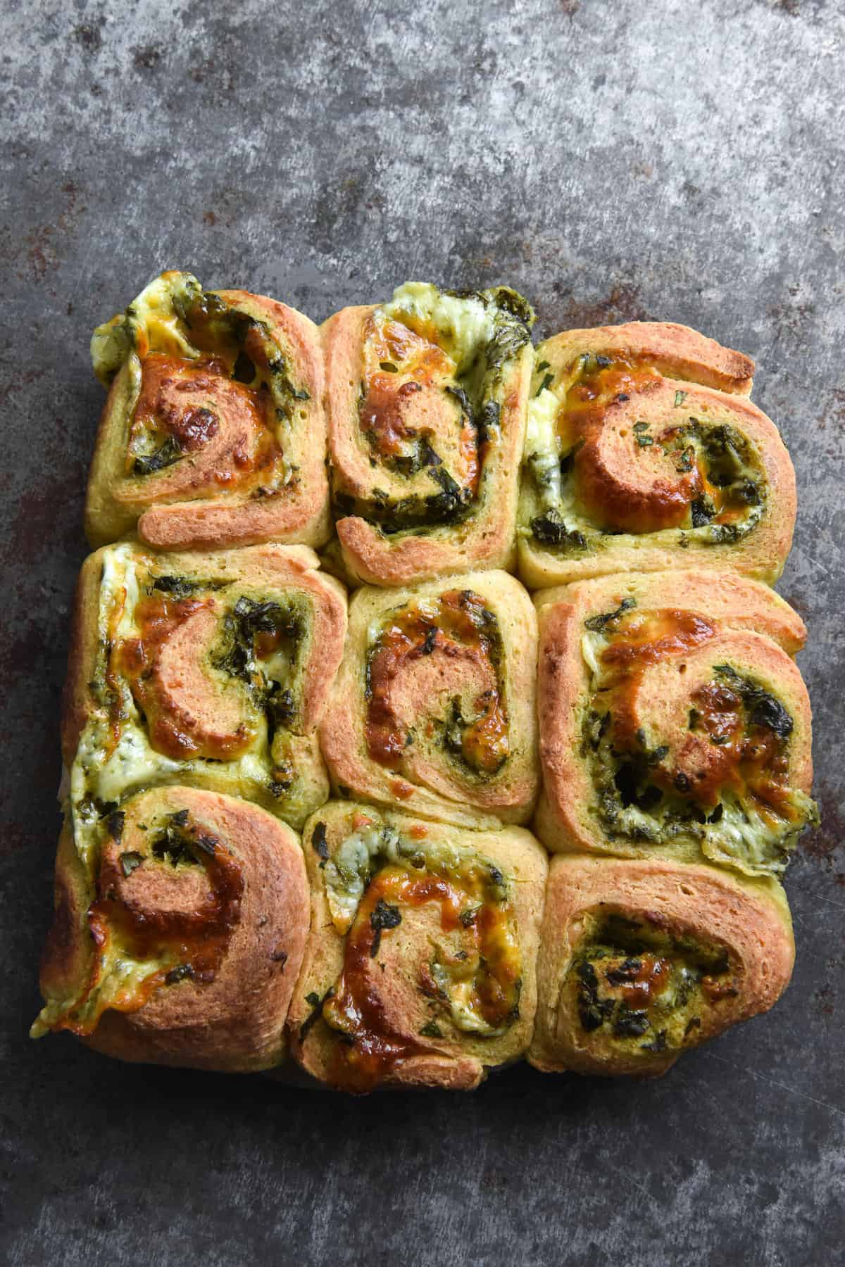 An aerial image of 9 gluten free pesto scrolls on a dark blue steel backdrop.