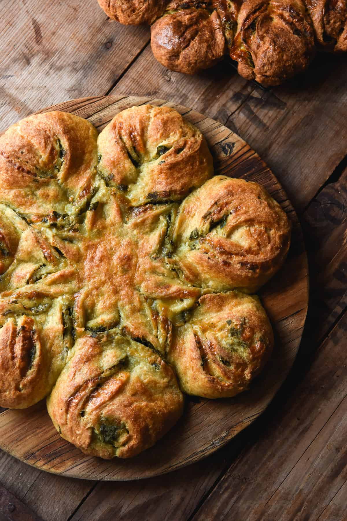 A gluten free pesto bread star sits atop a wooden board on a wooden backdrop in the bottom left corner of the image. A second pesto star sits in the top right hand corner of the image