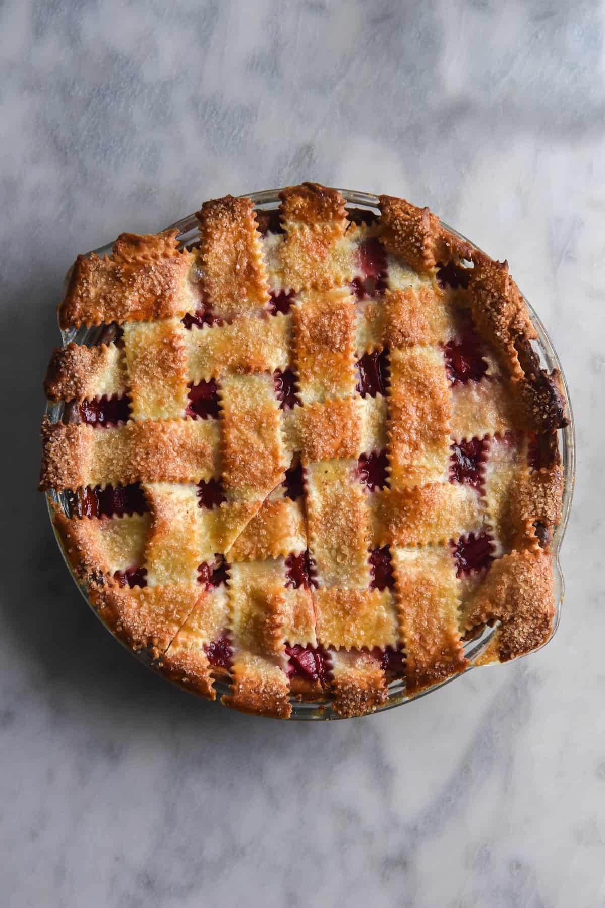A gluten free, FODMAP friendly strawberry and rhubarb lattice pie sits atop a white marble table in an aerial shot