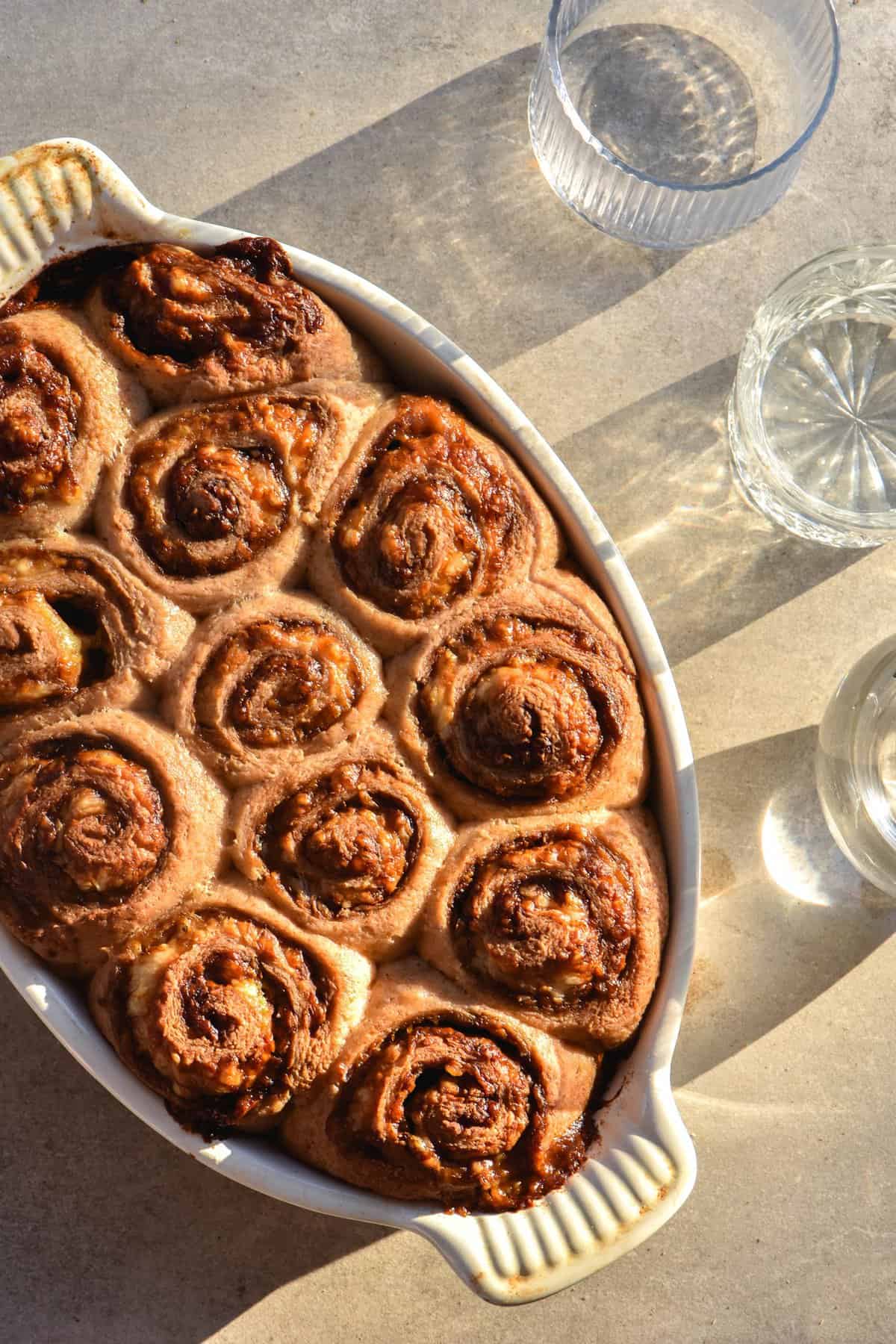 An aerial view of gluten free sourdough vegemite scrolls in harsh sunlight. Water glasses sit to the right of the image and create filtered light