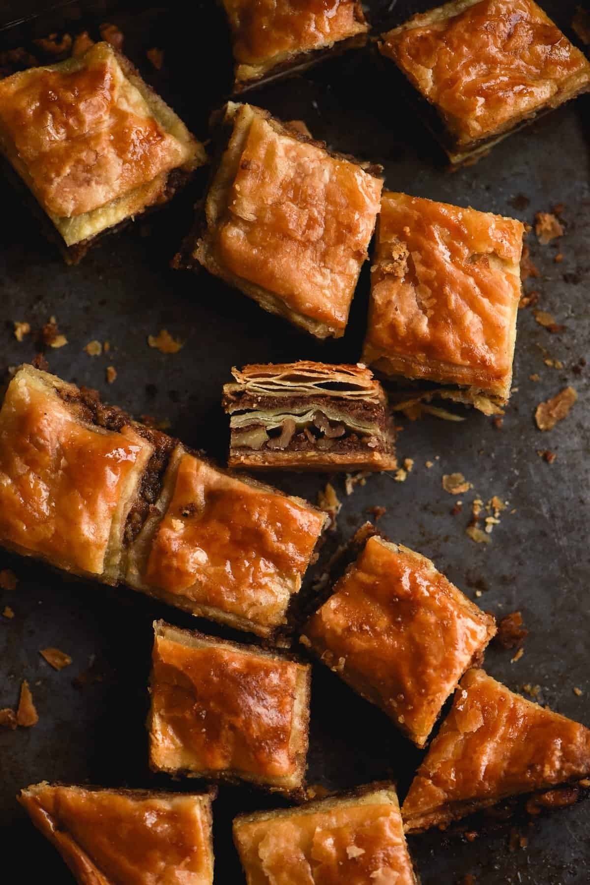 An aerial view of gluten free, FODMAP friendly baklava sits atop a dark grey backdrop. Some slices of baklava are tilted towards the camera to expose the layers and the nutty filling