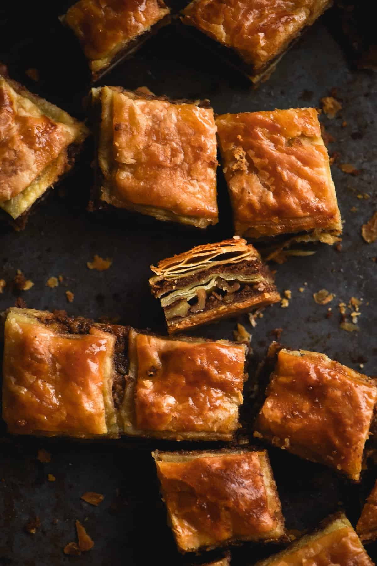 An aerial view of gluten free, FODMAP friendly baklava sits atop a dark grey backdrop. Some slices of baklava are tilted towards the camera to expose the layers and the nutty filling