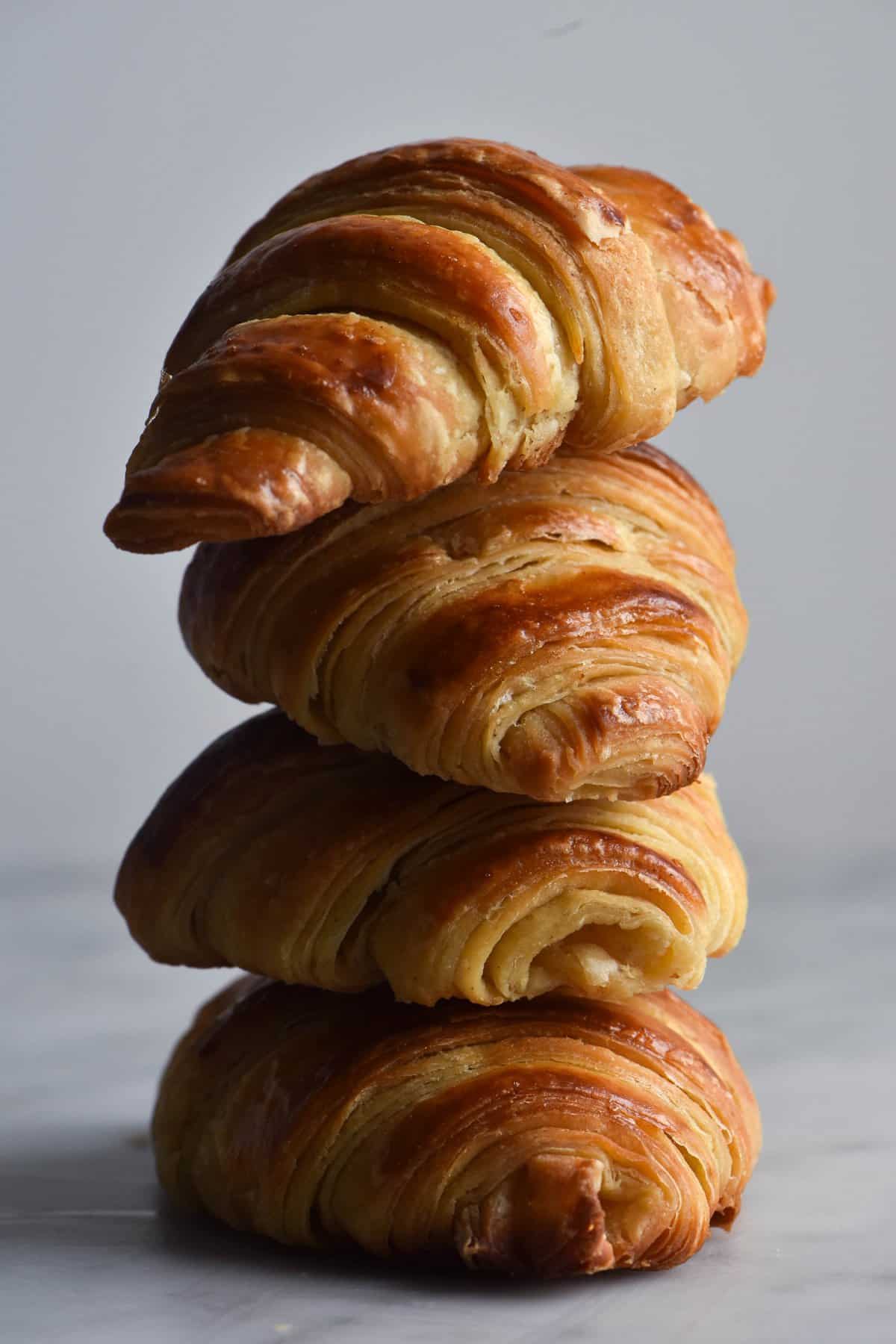 A stack of four gluten free croissants sits atop a white marble table against a white backdrop