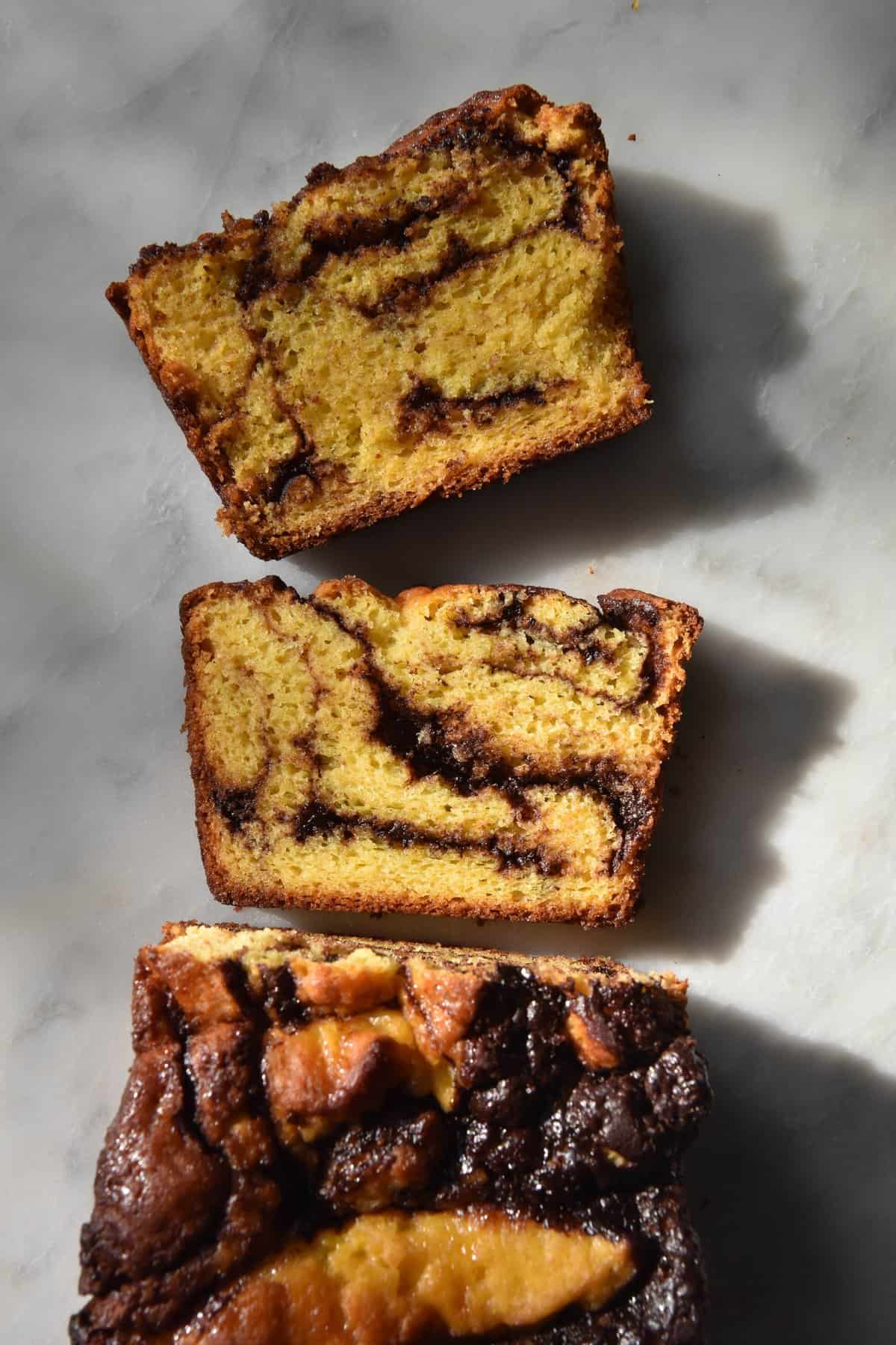 An aerial view of a gluten free, FODMAP friendly loaf of chocolate babka. The babka sits atop a white marble table and two slices face upwards to reveal the marbled chocolate innards