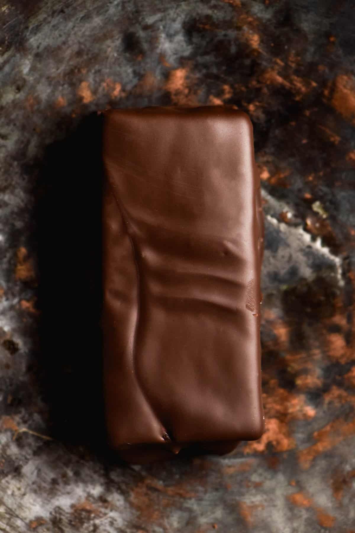 A close up aerial view of a gluten free homemade Tim Tam. It sits against a mottled grey and rust coloured backdrop