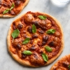 An aerial view of three gluten free sourdough pizza bases topped with FODMAP friendly pizza sauce and melty cheese. The pizzas sit in a diagonal pattern on the table and a glass of water sits in the top right hand side of the image