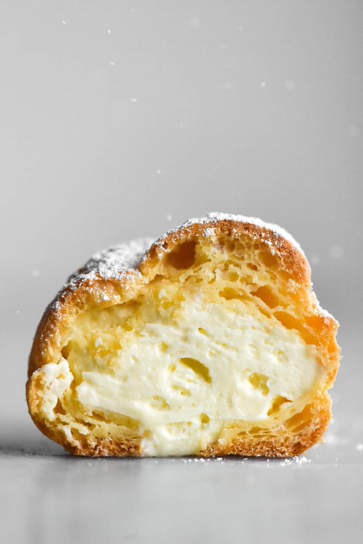 A side on macro view of a gluten free cream puff that has been sliced in half, exposing the whipped cream innards