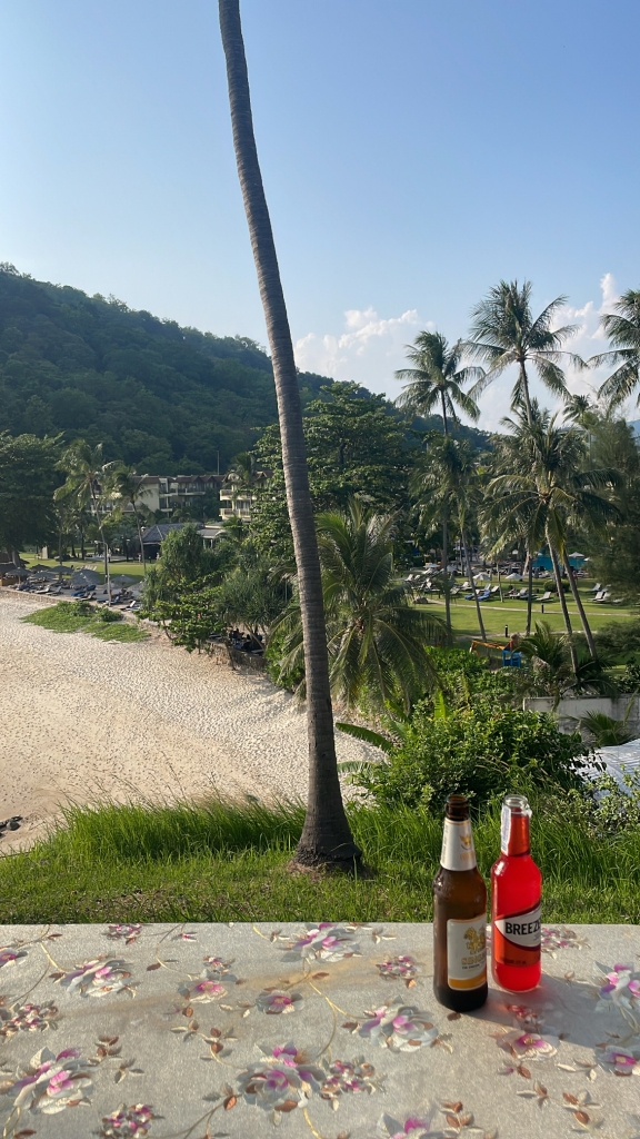 The view from Little Tiger Restaurant above Marriott Merlin Beach in Phuket. Two drinks sit on a table in the foreground and the beach and resort are in the background
