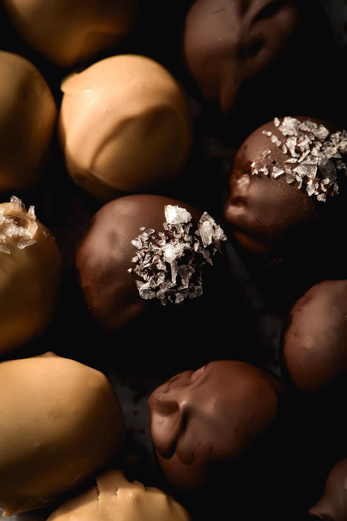 A close up, moody aerial photo of dark and white chocolate peanut butter truffles. The truffles are grouped together and some of them are sprinkled with sea salt flakes