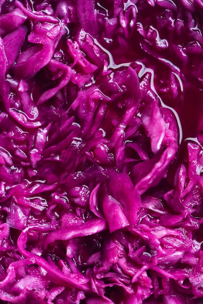 An aerial close up macro shot of FODMAP friendly 'pickled red onion'. The 'pickled red onion' is a vibrant purple and sitting casually in the pickling brine