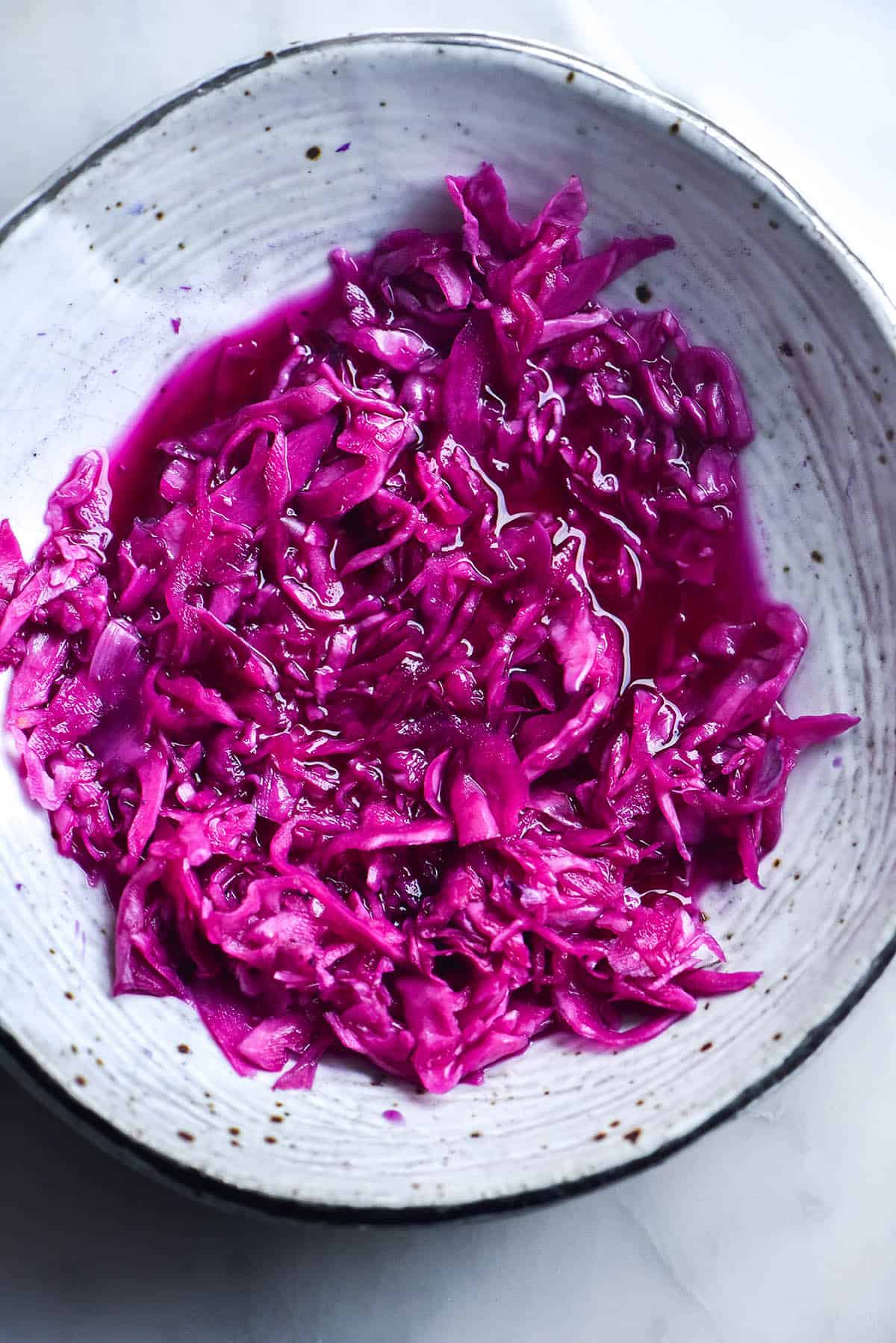 An aerial view of a white ceramic bowl filled with FODMAP friendly 'pickled red onion' in brine.