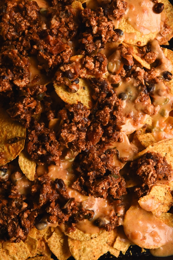 An aerial, close up view of a sheet tray of nachos, melty cheese and FODMAP friendly vegetarian chilli sin carne
