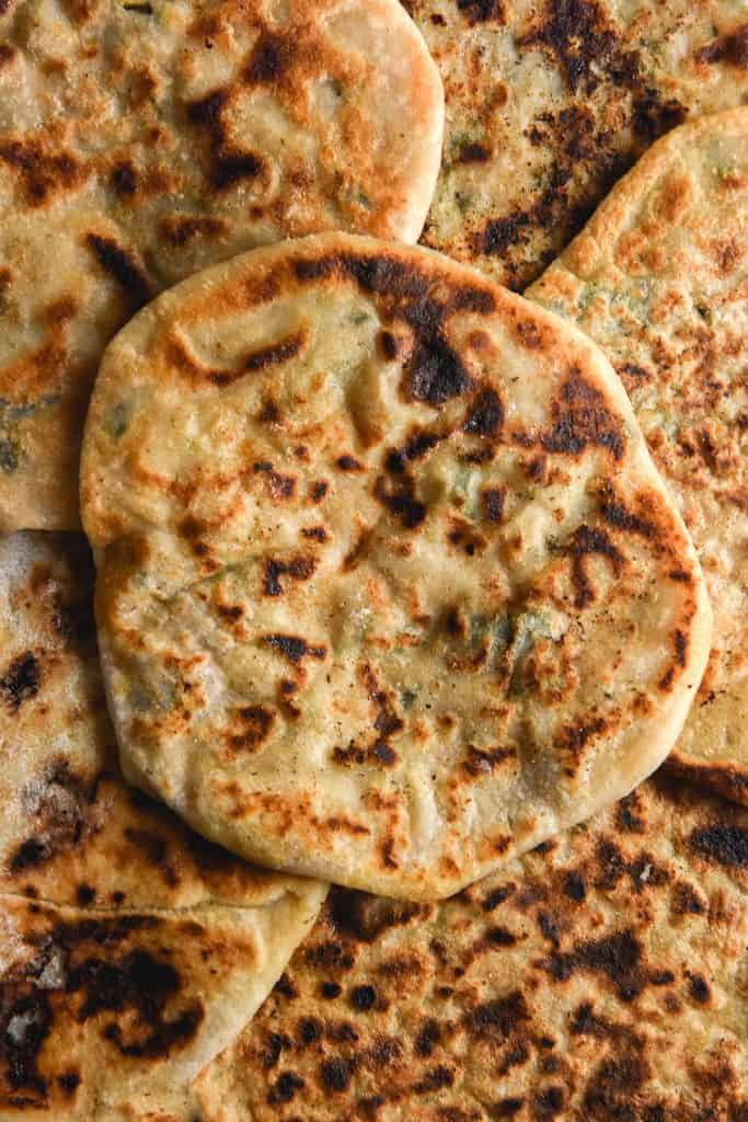 An aerial close up view of gluten free aloo paratha arrange so that you can't see the plate. The Aloo paratha are deeply golden and flecked with deep brown spots. Some of the herbs and chilli in the potato filling can be seen through the flatbread