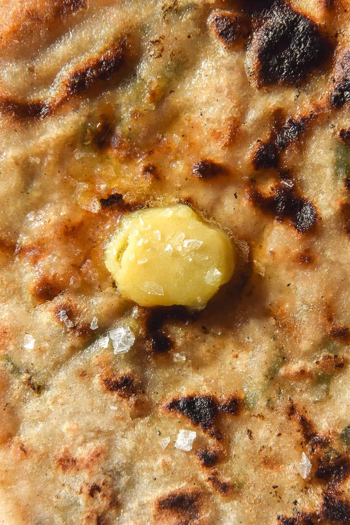 A close up of a gluten free Aloo Paratha topped with melting garlic infused ghee and sea salt flakes. 
