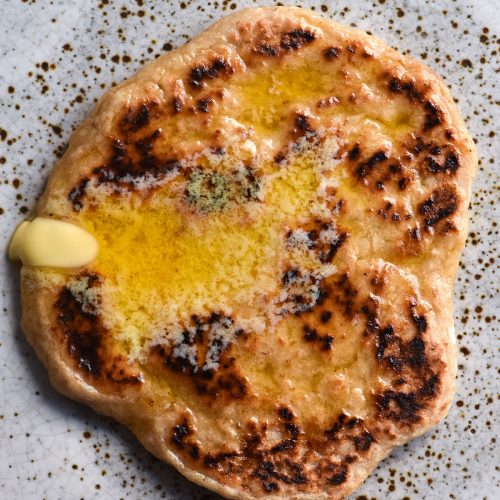 An aerial close up view of a gluten free yeasted flatbread topped with melted butter and sitting atop a white speckled ceramic plate