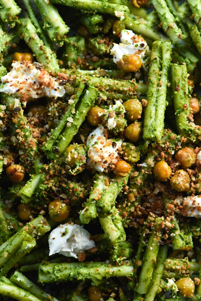 A close up macro aerial view of gluten free casarecce pasta smothered in FODMAP friendly pesto and topped with crispy roasted chickpeas, lemony breadcrumbs and homemade lactose free mascarpone