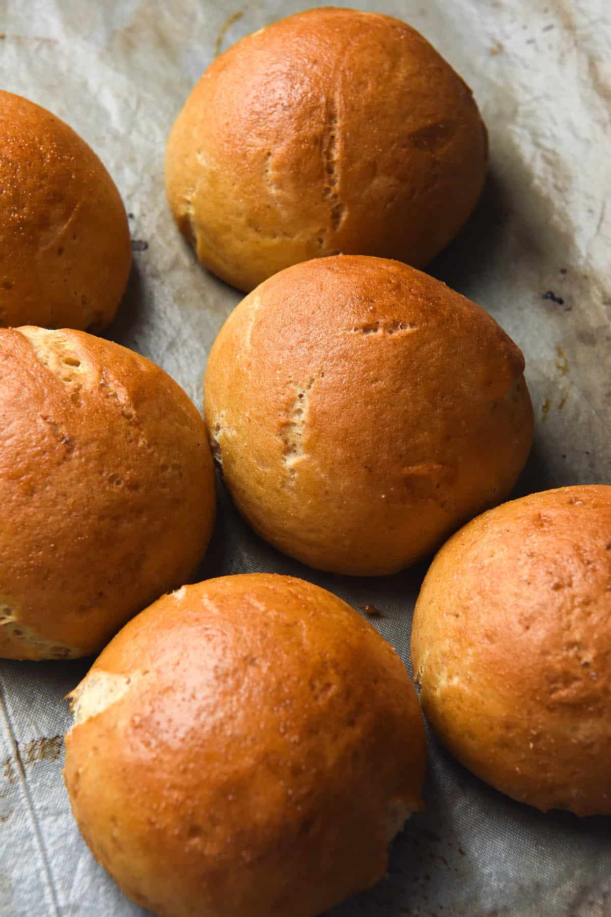 An aerial side on image of gluten free bread rolls atop a baking tray. The rolls are golden and perky and have small cracks from expanding in the oven.