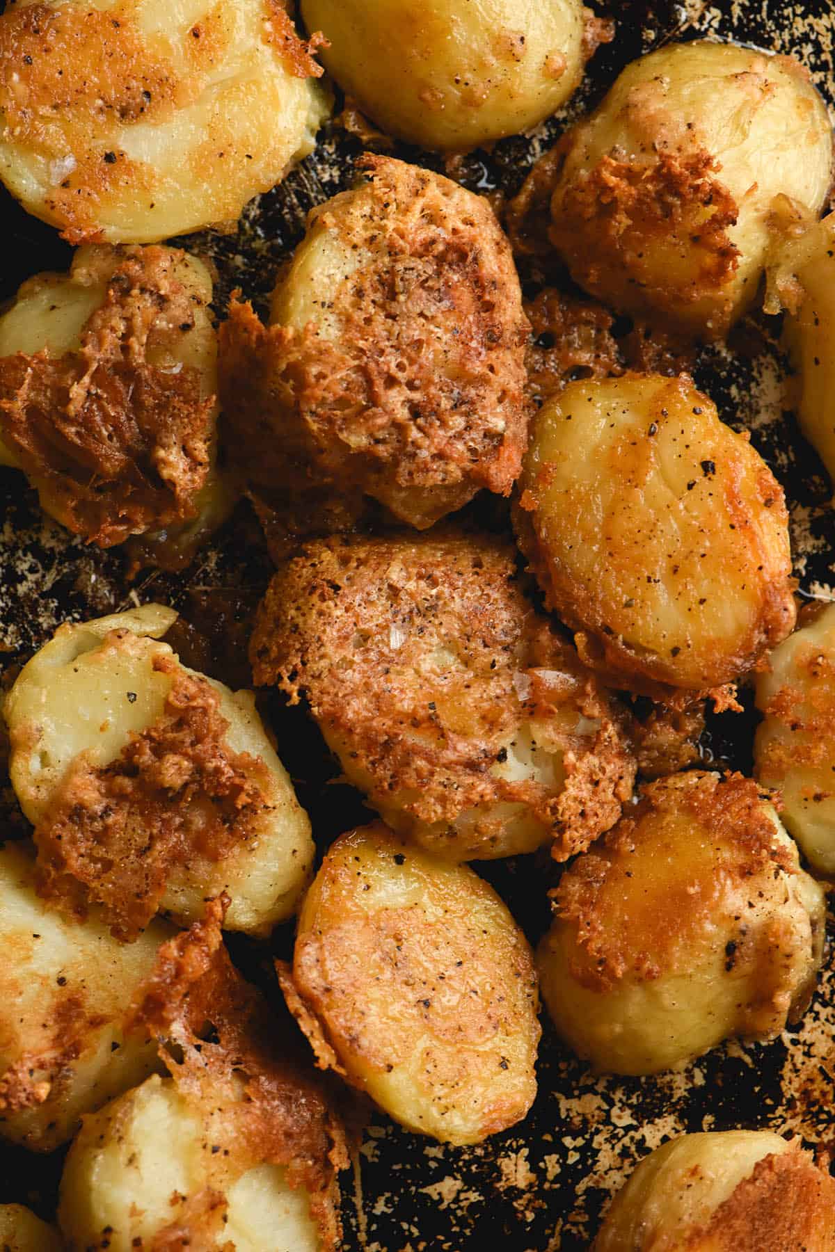 An aerial view of a dark baking tray covered with crispy cacio pepe potatoes. The potatoes are covered in crispy parmesan and speckled with pepper. 