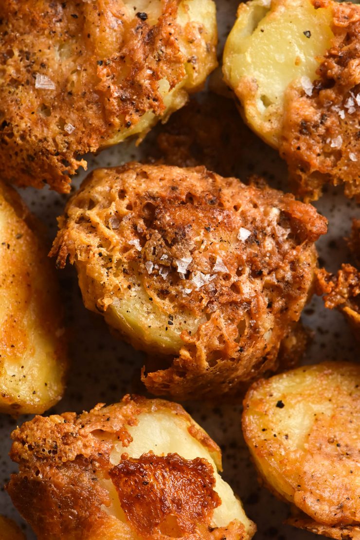 An aerial view of crispy cacio pepe roasted potatoes on a plate. They have a crispy parmesan and pepper crust and are sprinkled with sea salt flakes