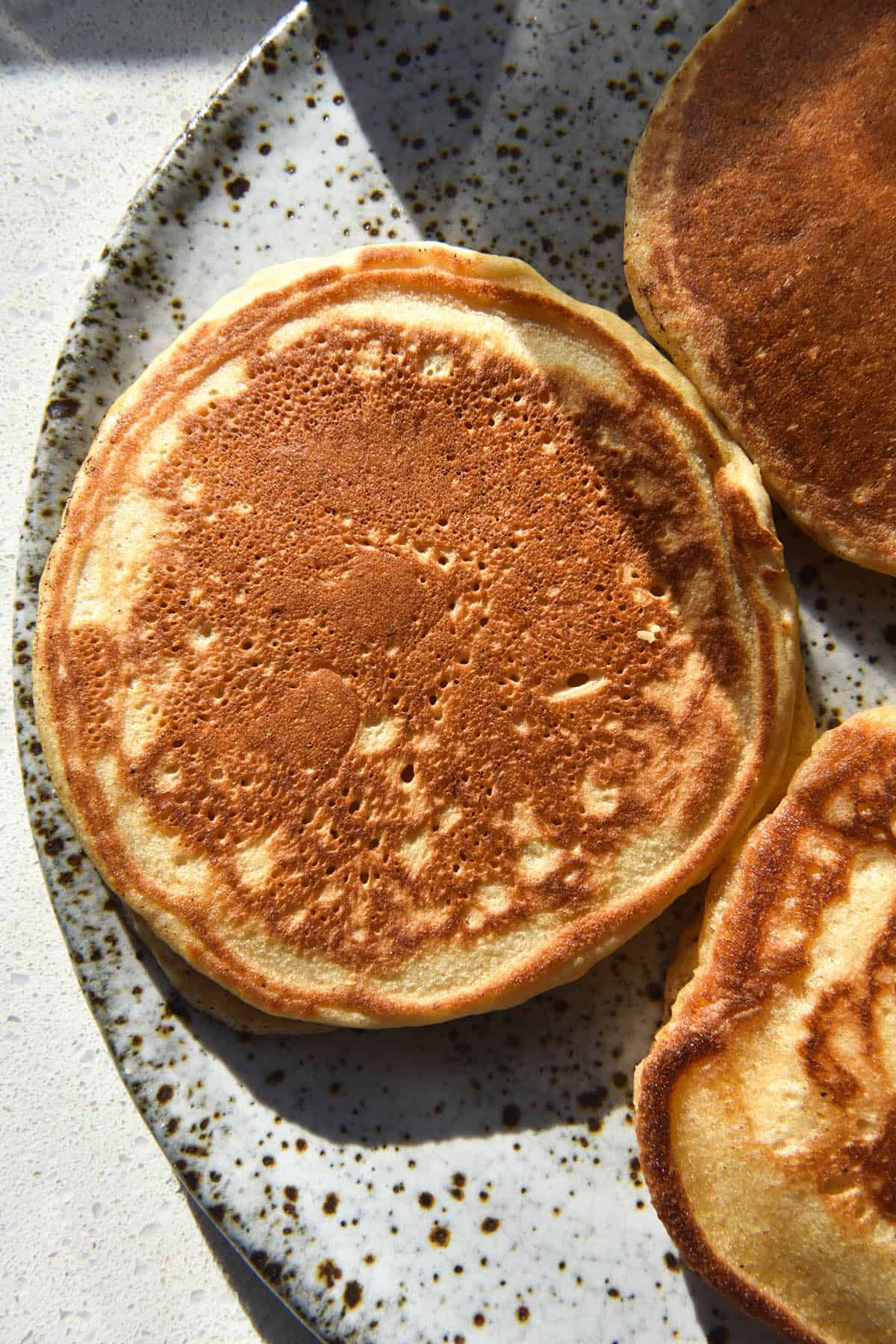 A close up aerial image of cassava flour pancakes on a white speckled ceramic plate. The pancakes sit in bright sunlight which adds contrasting light to the right side of the image.