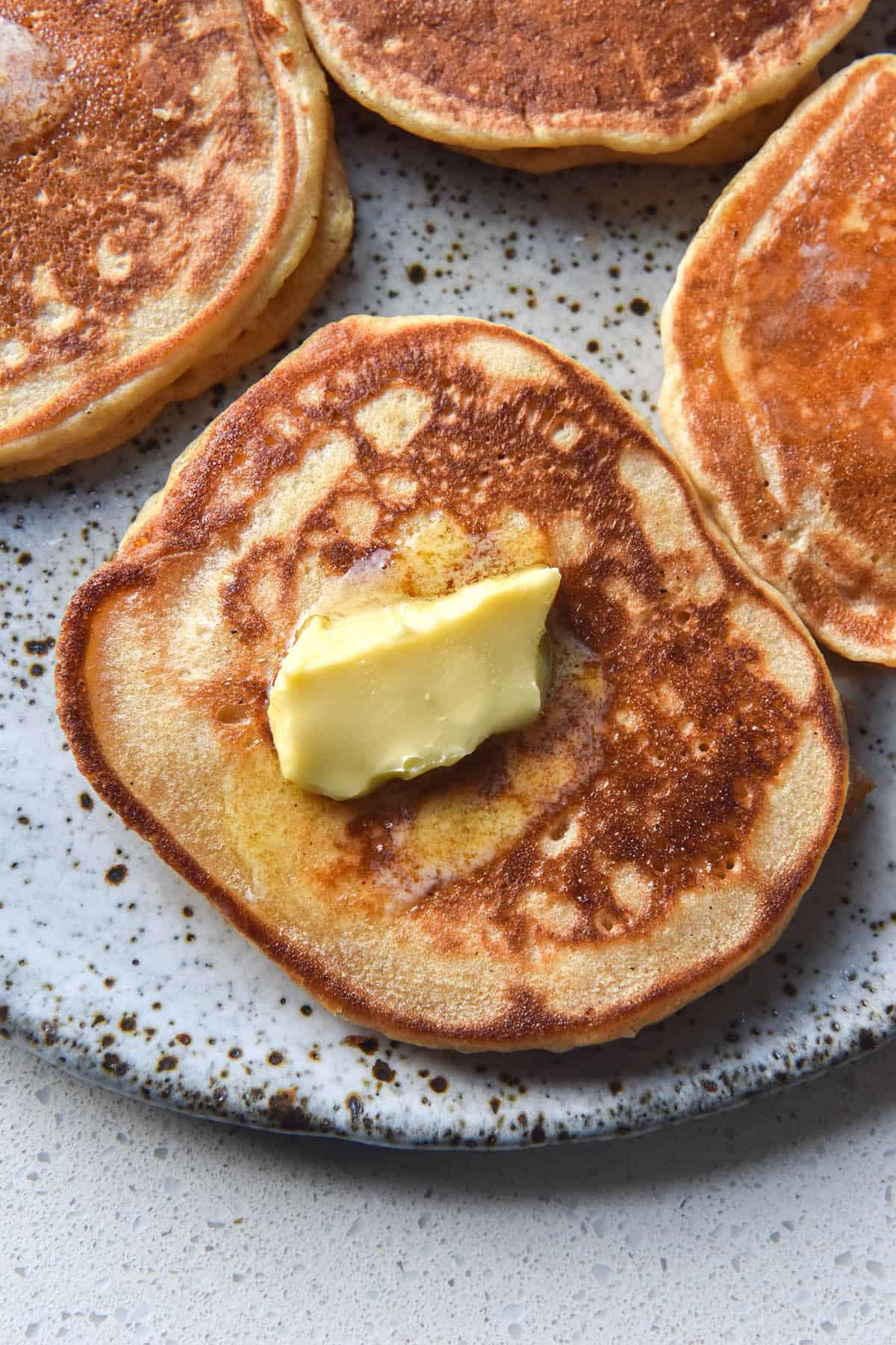 An aerial close up view of a white speckle ceramic plate topped with cassava flour pancakes. The pancakes are speckled golden brown, and the pancake in the forefront of the image is topped with melting butter. 