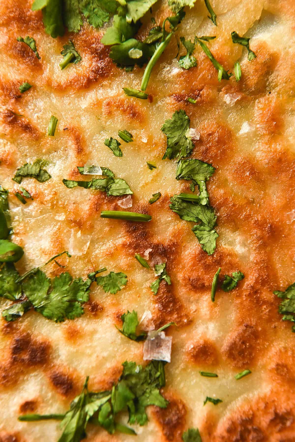 A close up image of a gluten free cheesy naan topped with garlic infused ghee, chopped parsley and sea salt flakes. 