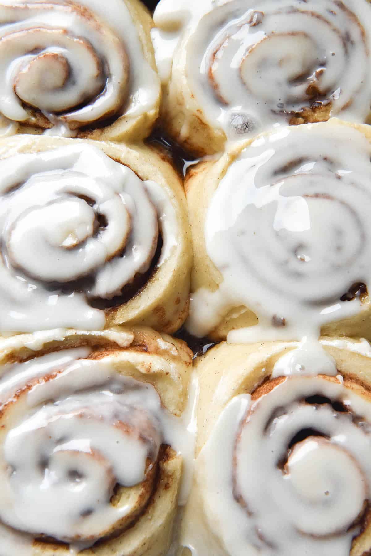 An aerial close up view of a tray of six gluten free, vegan cinnamon scrolls. The scrolls are snug together and drizzled with a vegan glaze that melts into the swirls 