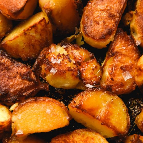 An aerial view of a baking tray topped with crispy roasted potatoes. The potatoes are golden brown and some of them have been finished with sea salt flakes