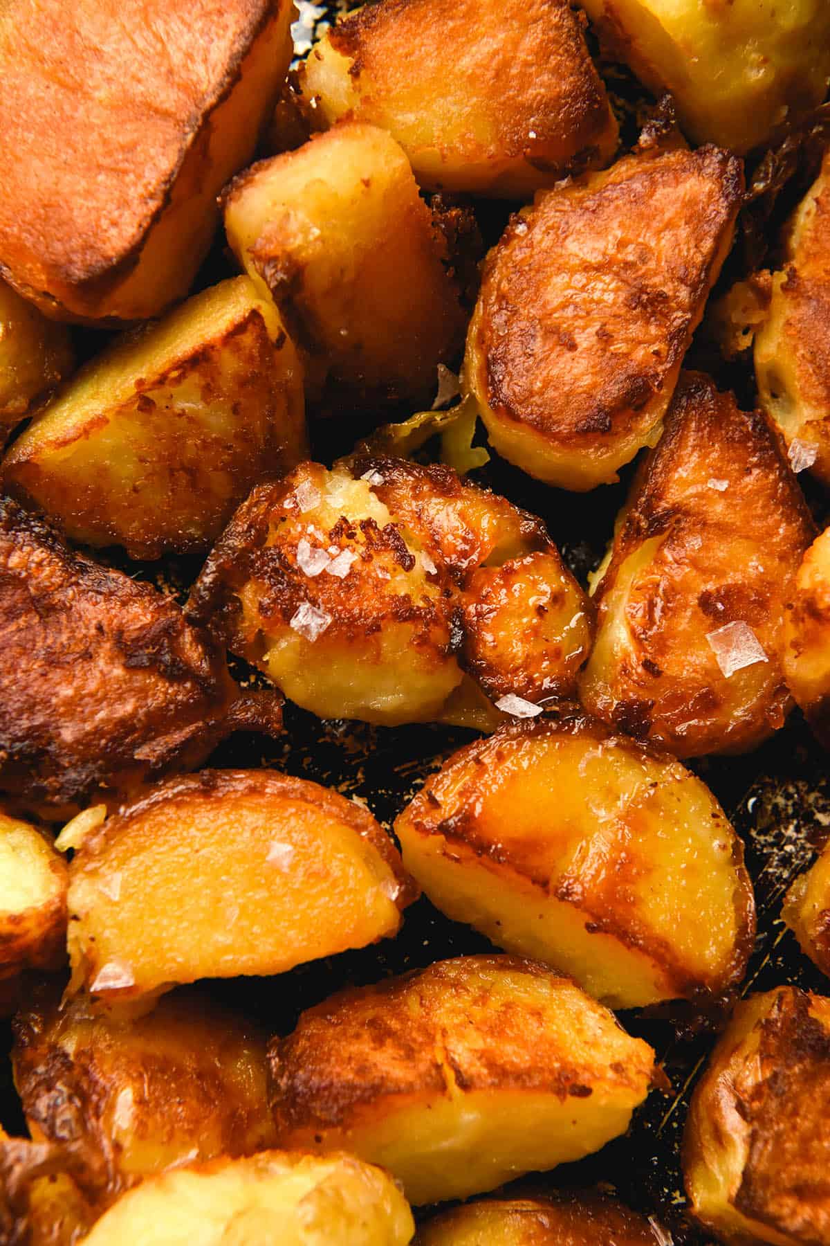 An aerial view of a baking tray topped with crispy roasted potatoes. The potatoes are golden brown and some of them have been finished with sea salt flakes