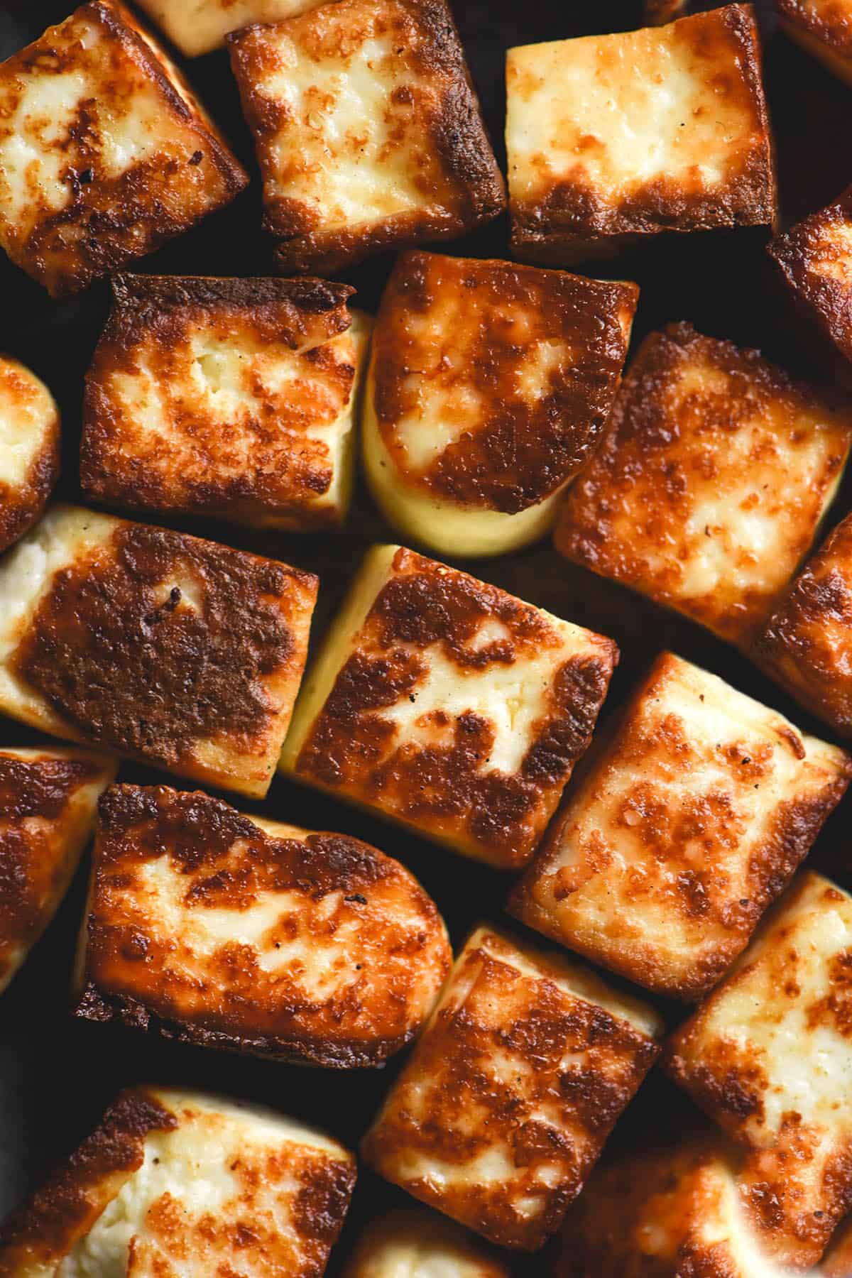 A close up macro photo of golden brown squares of fried lactose free paneer.