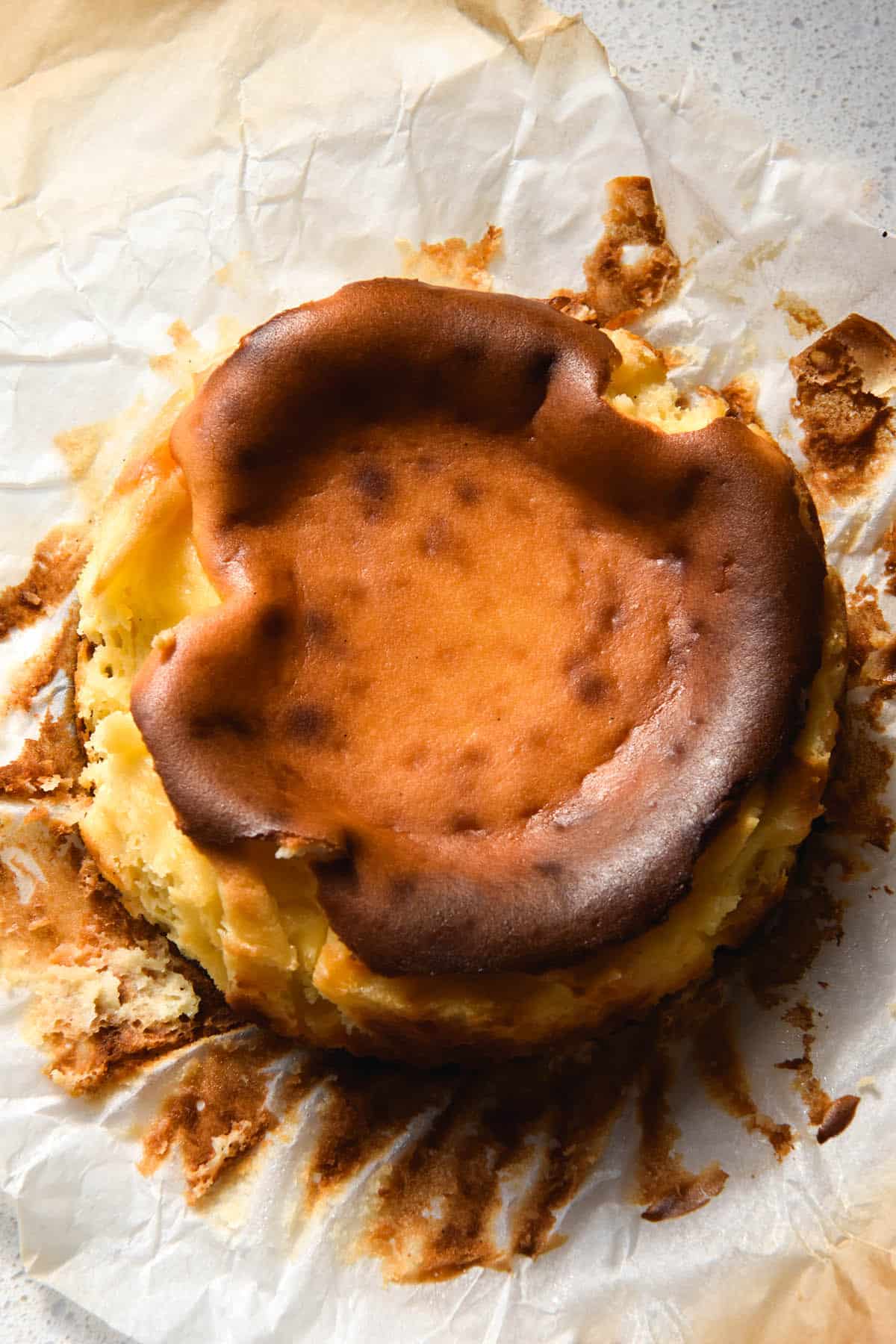 An aerial view of a mini Basque cheesecake. The top of the cheesecake is caramelised and the baking paper has been pulled away from the sides, forming the background of the image