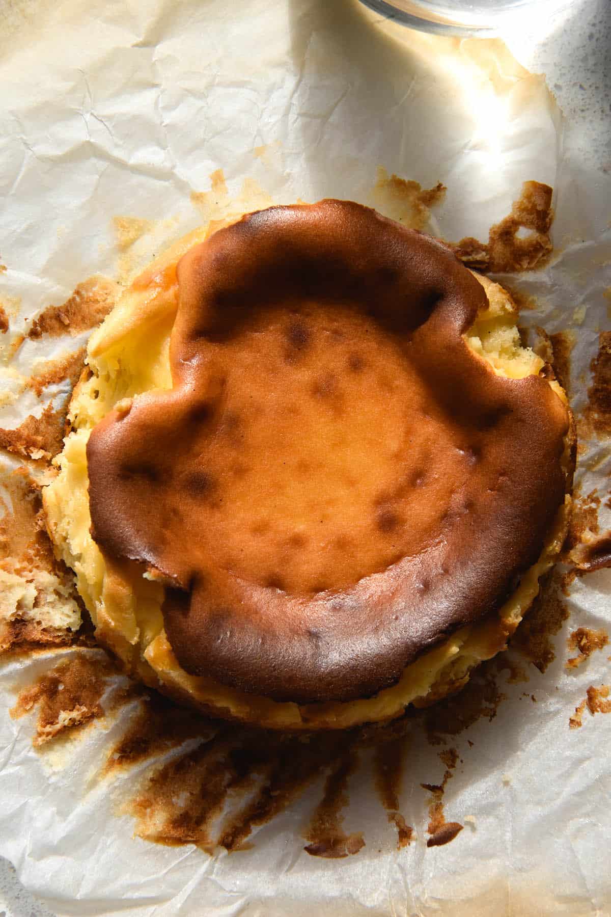 An aerial view of a mini Basque cheesecake. The top of the cheesecake is caramelised and the baking paper has been pulled away from the sides, forming the background of the image