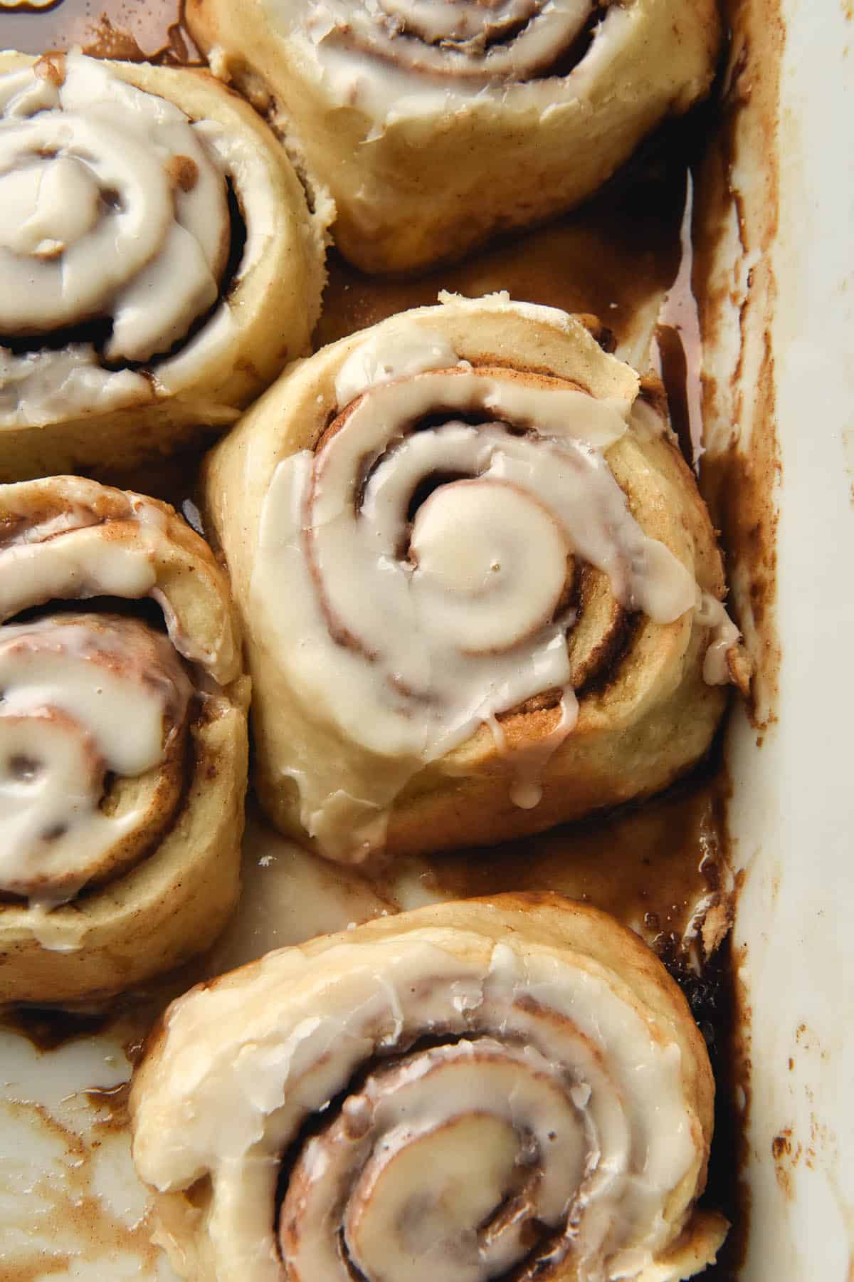 An aerial photo of vegan, gluten free, yeast free cinnamon scrolls topped with a vegan icing. The scrolls sit in a white baking dishes and are casually strewn. 