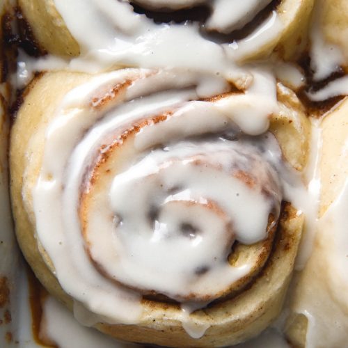 An aerial close up image of gluten free, vegan cinnamon scrolls in a baking dish. The scrolls are topped with a sugary glaze.