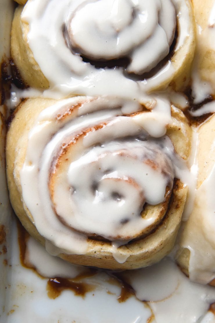 An aerial close up image of gluten free, vegan cinnamon scrolls in a baking dish. The scrolls are topped with a sugary glaze.