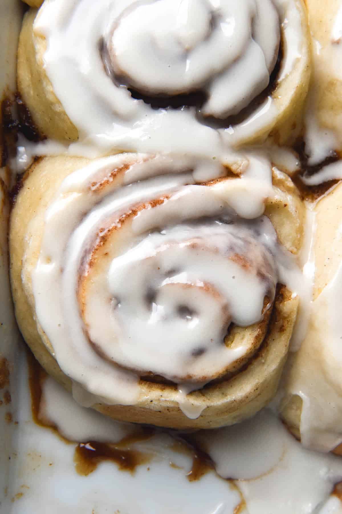 An aerial close up image of gluten free cinnamon scrolls in a baking dish. The scrolls are topped with a sugary glaze.