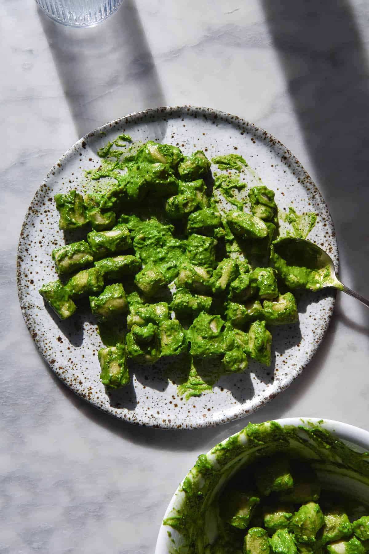 An aerial, sunlit image of a white speckled plate topped with gluten free gnocchi smothered in FODMAP friendly kale pesto. 