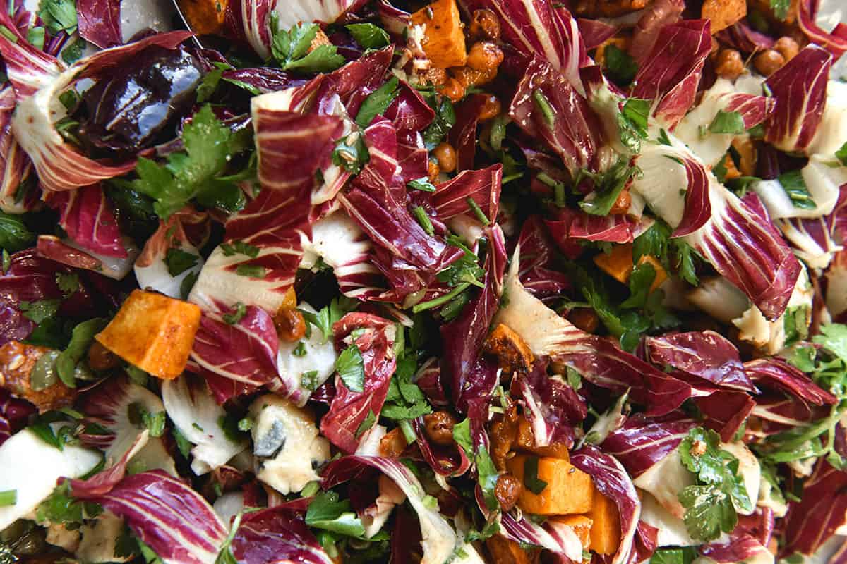 A close up photo of a radicchio salad with roasted pumpkin, parsley, smoky chickpeas and blue cheese. It is dressed with an oil based dressing and topped with toasted fennel seeds, which rest atop chopped pieces of radicchio.