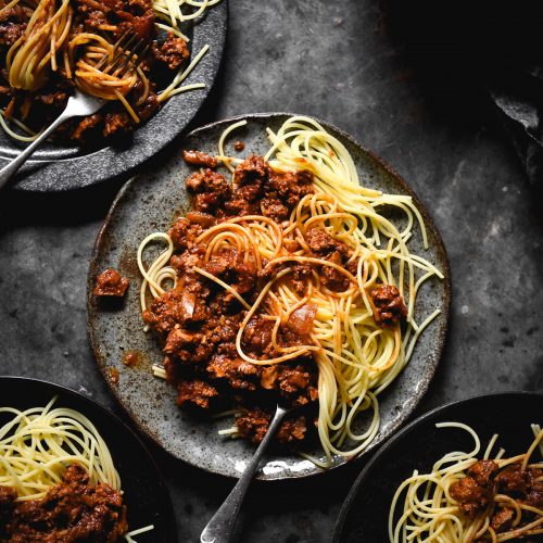 An aerial view of four plates of FODMAP friendly vegan bolognese on dark blue ceramic plates against a dark blue steel backdrop