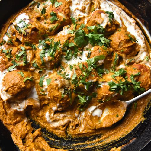 An aerial close up view of a black skillet filled with FODMAP friendly Malai kofta topped with a swirl of cream and chopped coriander
