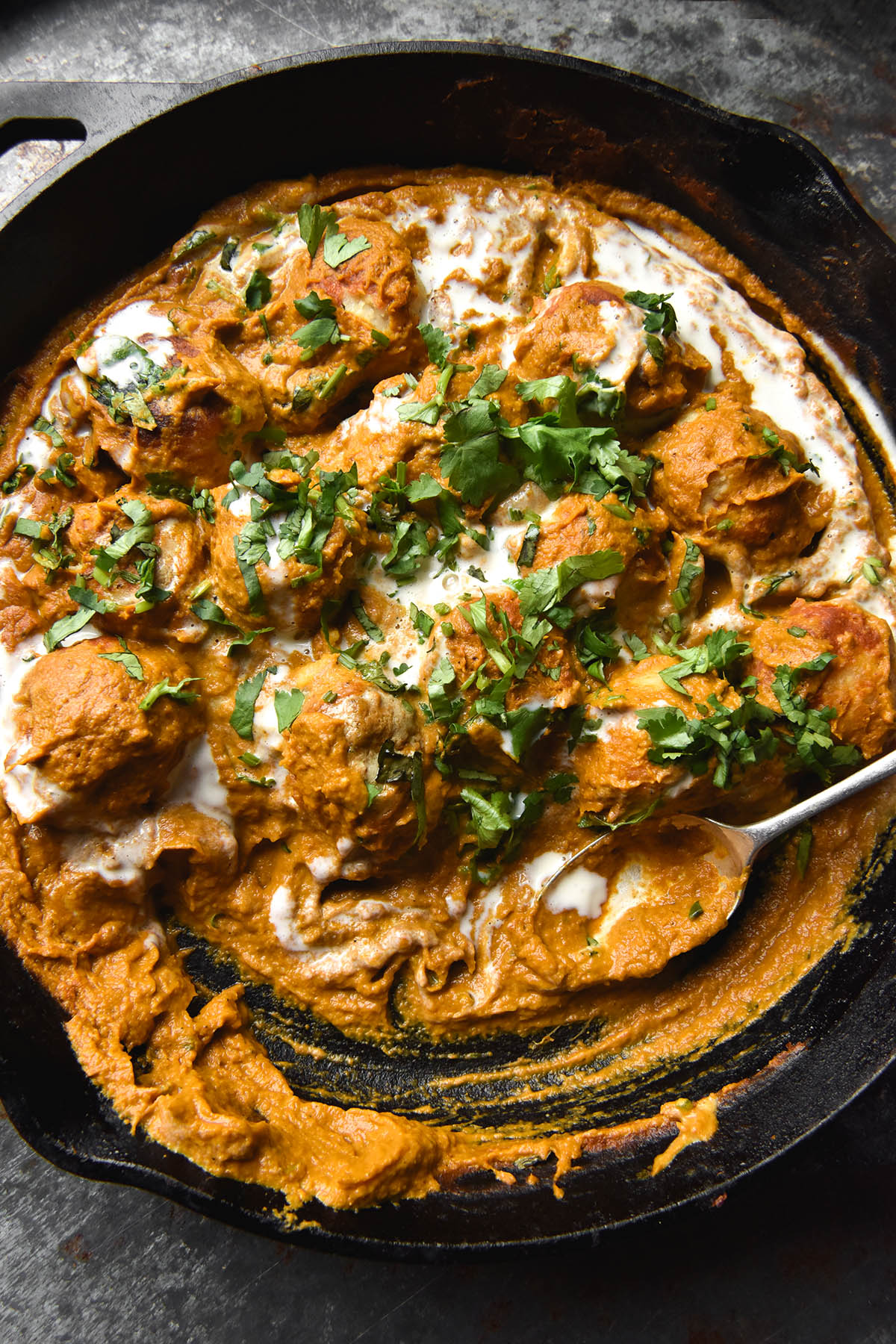 An aerial close up view of a black skillet filled with FODMAP friendly Malai kofta topped with a swirl of cream and chopped coriander