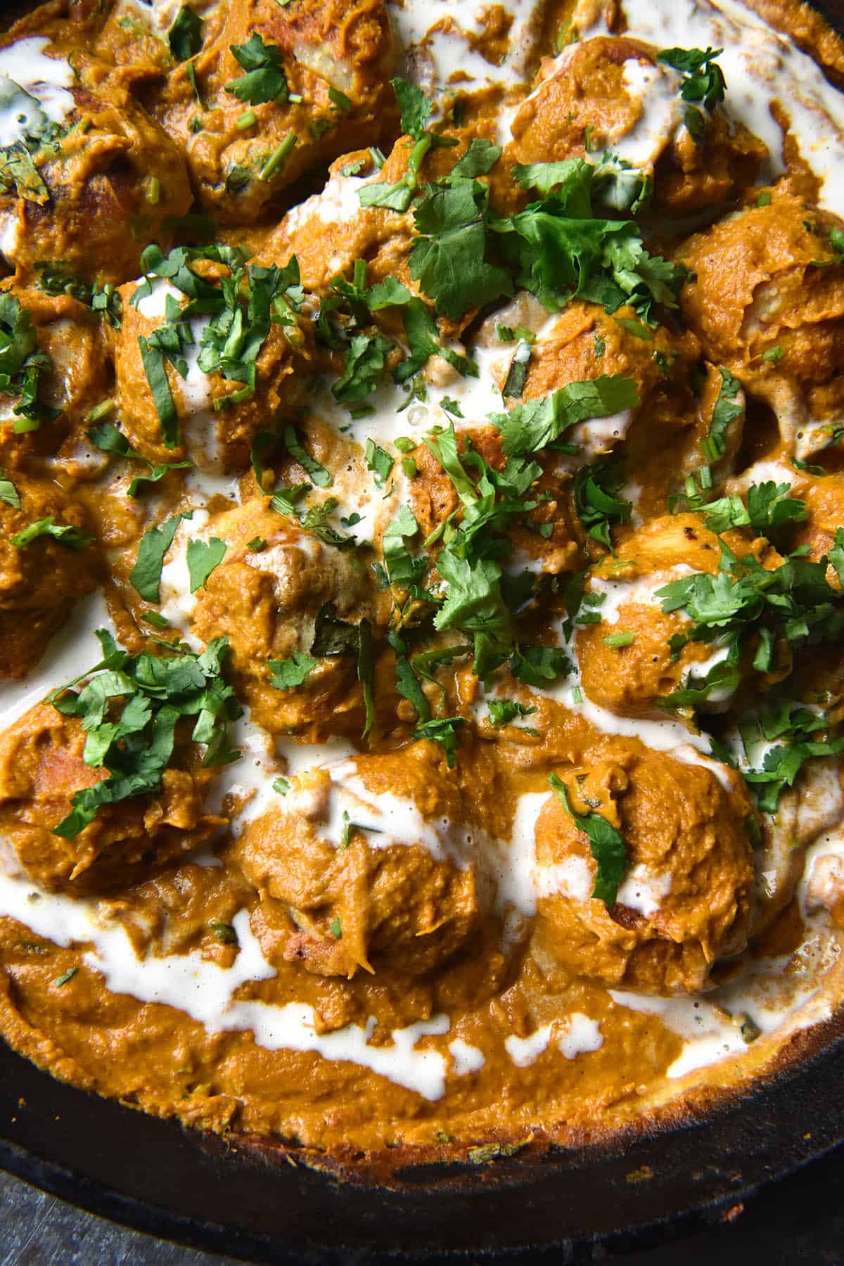 An aerial close up view of a skillet filled with FODMAP friendly Malai kofta. The Malai kofta sits in a black skillet topped with cream and coriander 