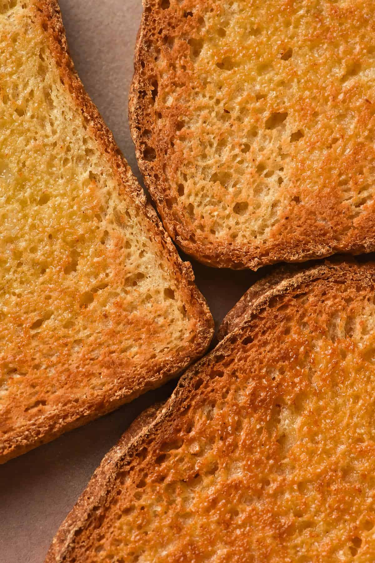 An aerial close up photo of three pieces of golden brown toasted grain free bread on a pale pink ceramic plate. The toast has been slathered with butter which has melted into the crumb