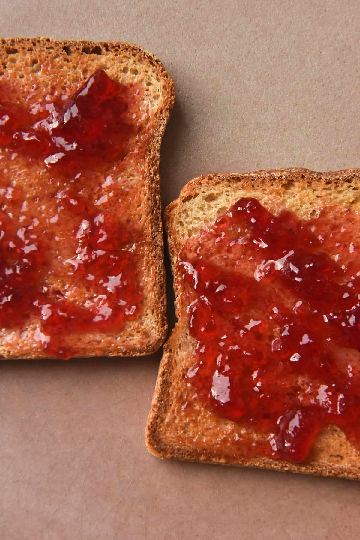 A close up aerial view of two pieces of grain free bread toasted and topped with raspberry jam. The toast sits on a pale pink textured ceramic plate. 